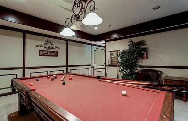 Une table de billard avec des billes, un lustre et un mur orné d’une enseigne décorative.