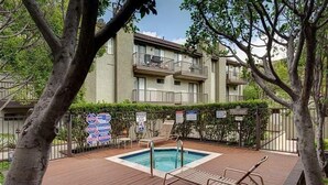 A pool area with a wooden deck, lounge chairs, and a building with balconies in the background. - Heart of Pasadena - Walkable/Bikeable to hospitals, Old Town and Caltech/PCC (Pasadena)