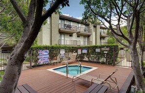 A pool area with a wooden deck, lounge chairs, and a building with balconies in the background. - Heart of Pasadena - Walkable/Bikeable to hospitals, Old Town and Caltech/PCC (Pasadena)