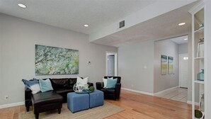 A spacious living room with a dark leather sofa, a blue ottoman, and a large abstract painting on the wall. - Heart of Pasadena - Walkable/Bikeable to hospitals, Old Town and Caltech/PCC (Pasadena)