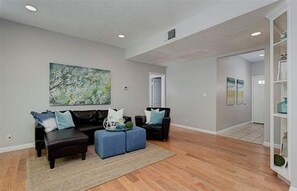 A spacious living room with a dark leather sofa, a blue ottoman, and a large abstract painting on the wall. - Heart of Pasadena - Walkable/Bikeable to hospitals, Old Town and Caltech/PCC (Pasadena)