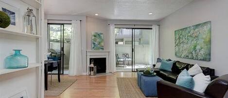 A living room with a fireplace, a sofa, and a dining area visible through glass doors.
