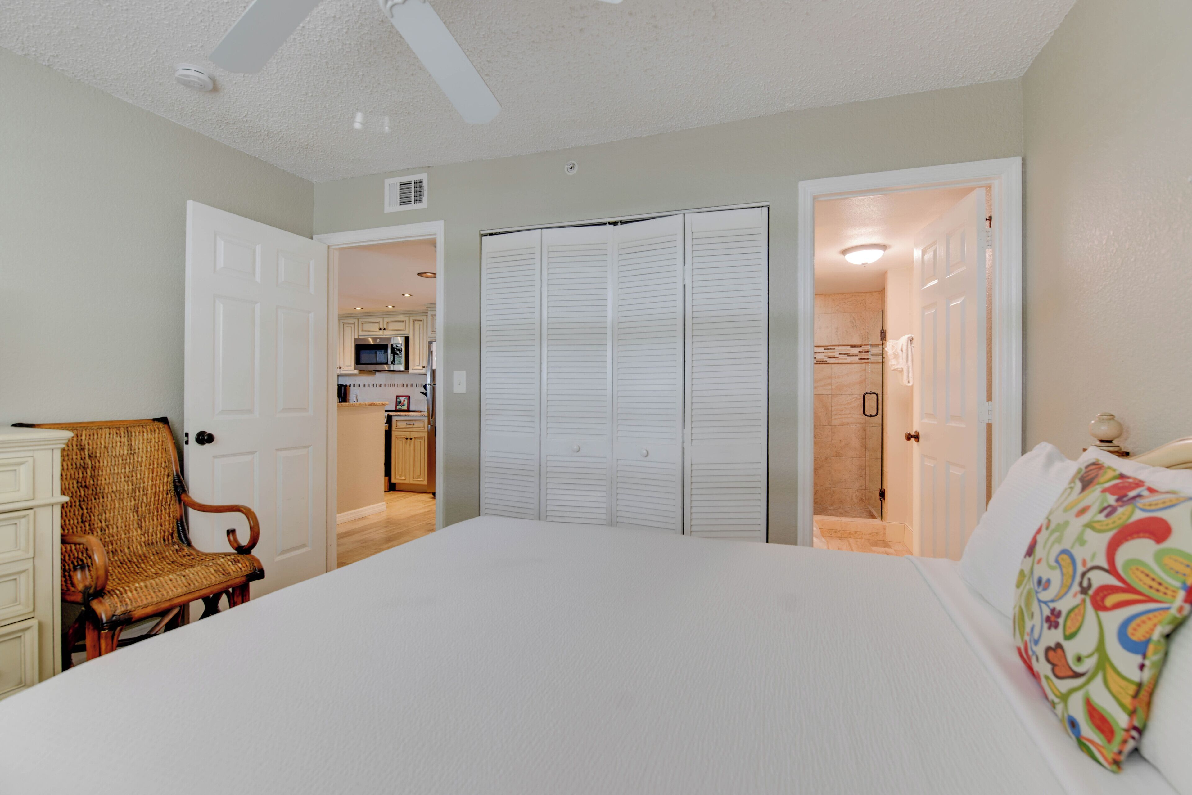 A bedroom with a bed, a chair, a wardrobe, and a bathroom visible through an open door.
