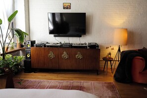 Un salon avec un téléviseur à écran plat fixé sur un mur en briques blanches, un meuble en bois contenant des platines, un haut-parleur et une lampe.