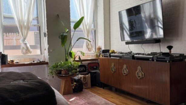Een slaapkamer met een bed, een televisie, een houten dressoir en een raam met gordijnen.