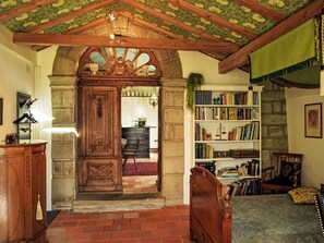Una habitació amb una porta de fusta, una estant, un llit i un paviment de maó.