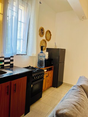 Eine kleine Küche mit Herd, Backofen, Kühlschrank und Wasserspender.