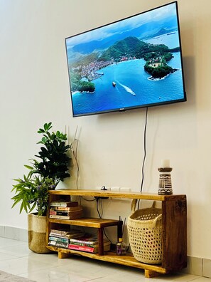 Ein Flachbildfernseher an einer Wand über einem Holztisch mit Büchern und Dekorationsobjekten.