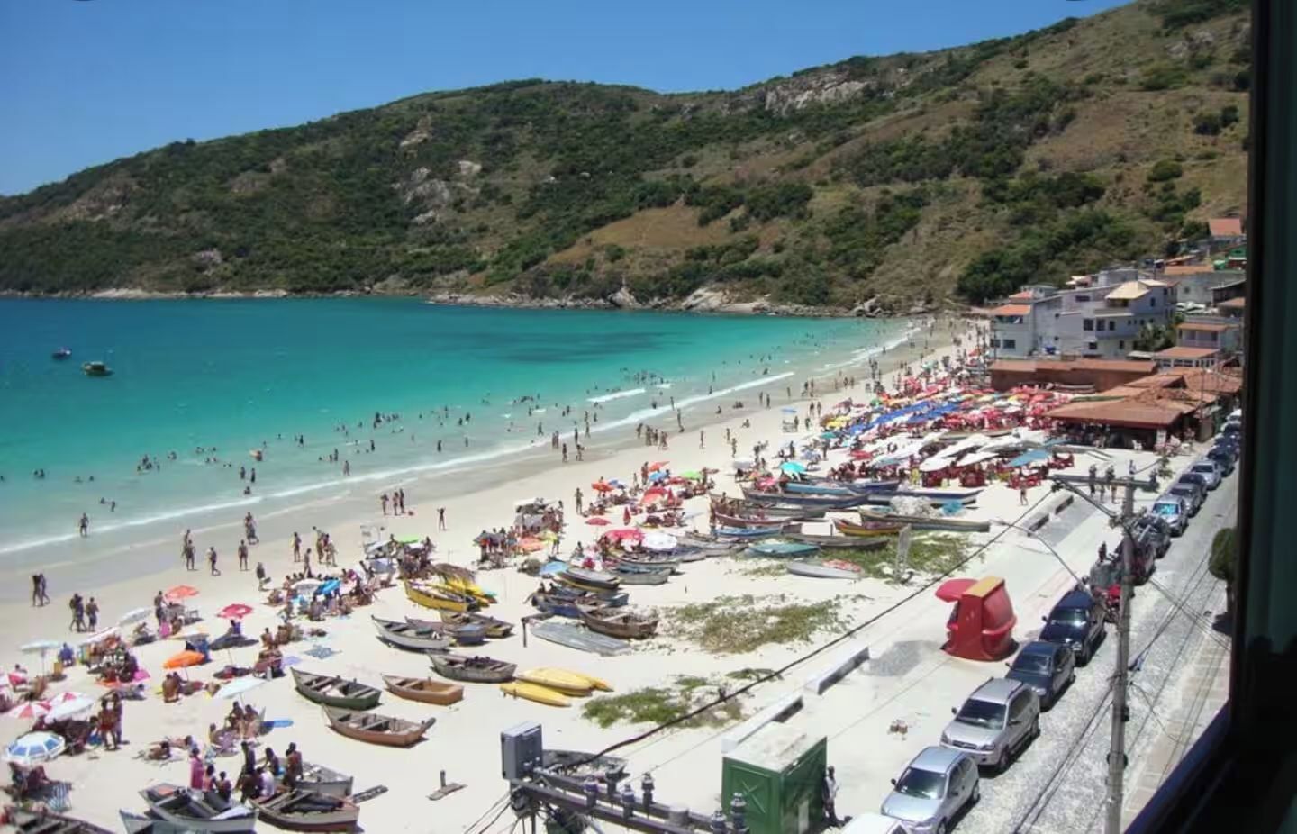 A beach with boats, umbrellas, and buildings in the background.