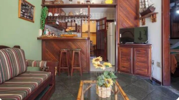 Un soggiorno con divano, tavolino da caffè con fiori, angolo cottura con bancone e televisione su un mobiletto.