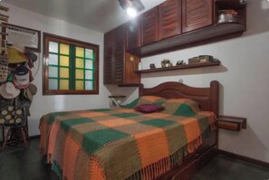 Ein Schlafzimmer mit einem hölzernen Bett, einem Fenster mit grün-gelben Fenstern und einem Regal über dem Bett.