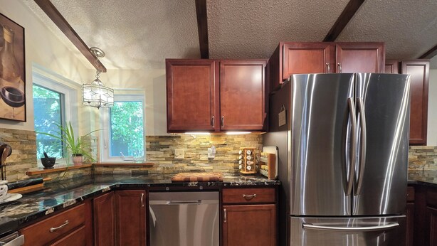A kitchen with wooden cabinets, a stainless steel refrigerator, a dishwasher, and a stone backsplash.