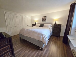 A bedroom with a bed, bedside lamps, a dresser, and a door.