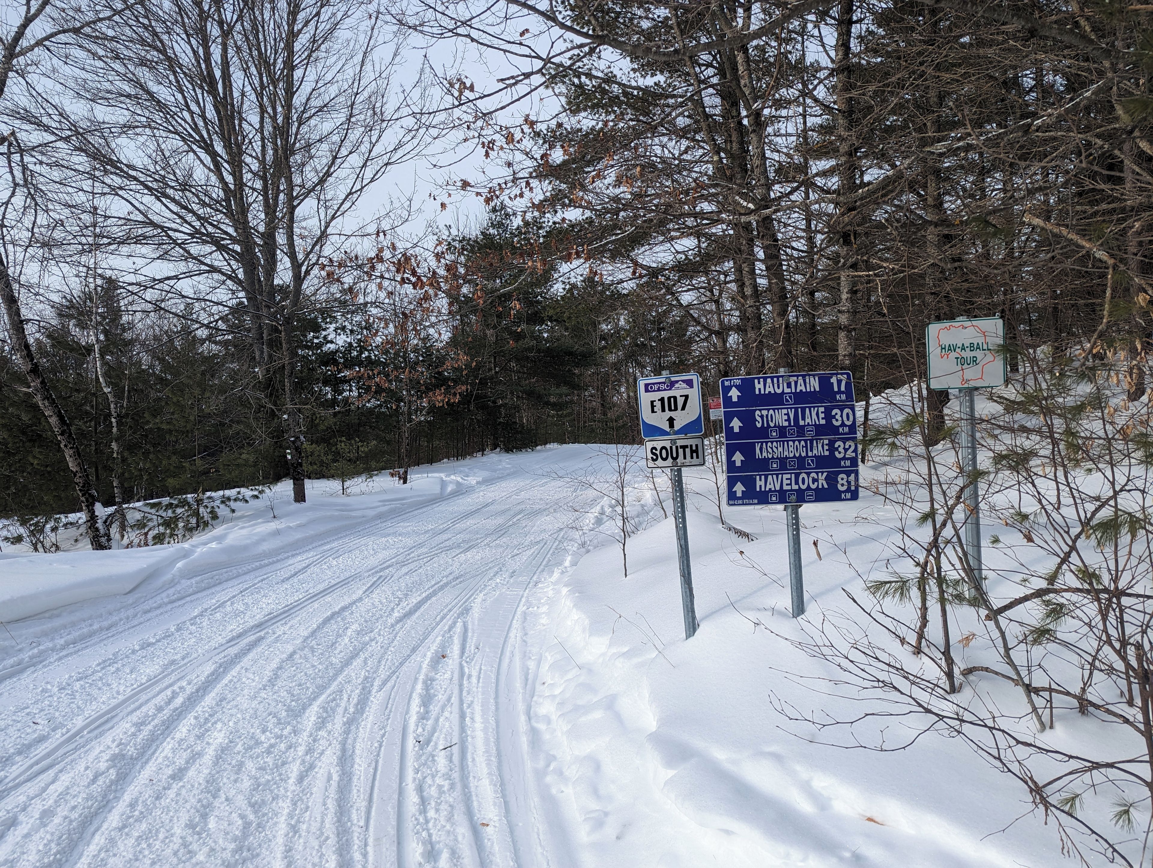 A snow-covered road with directional signs for E107 South and a Havelock tour.