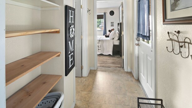 A hallway with wooden shelves, a 'HOME' sign, a door with a blue curtain, and a framed picture on the wall. - Fire Pit Backyard, Walk to Town, Close to Glacier, Whitefish,Ski Hill, Northfork (Columbia Falls)