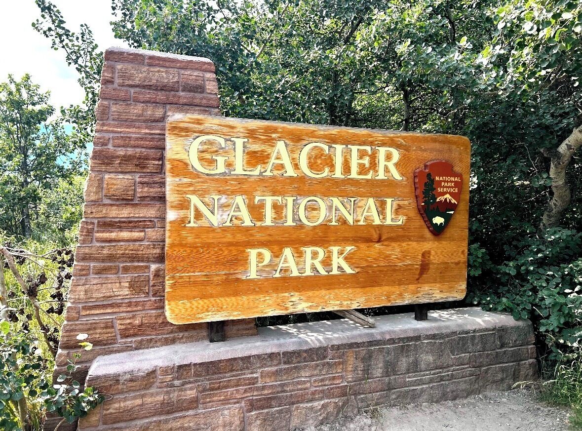 A wooden sign for Glacier National Park with a bear emblem.