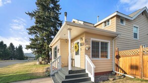 A two-story house with a front porch, a wooden fence, and a driveway. - Fire Pit Backyard, Walk to Town, Close to Glacier, Whitefish,Ski Hill, Northfork (Columbia Falls)