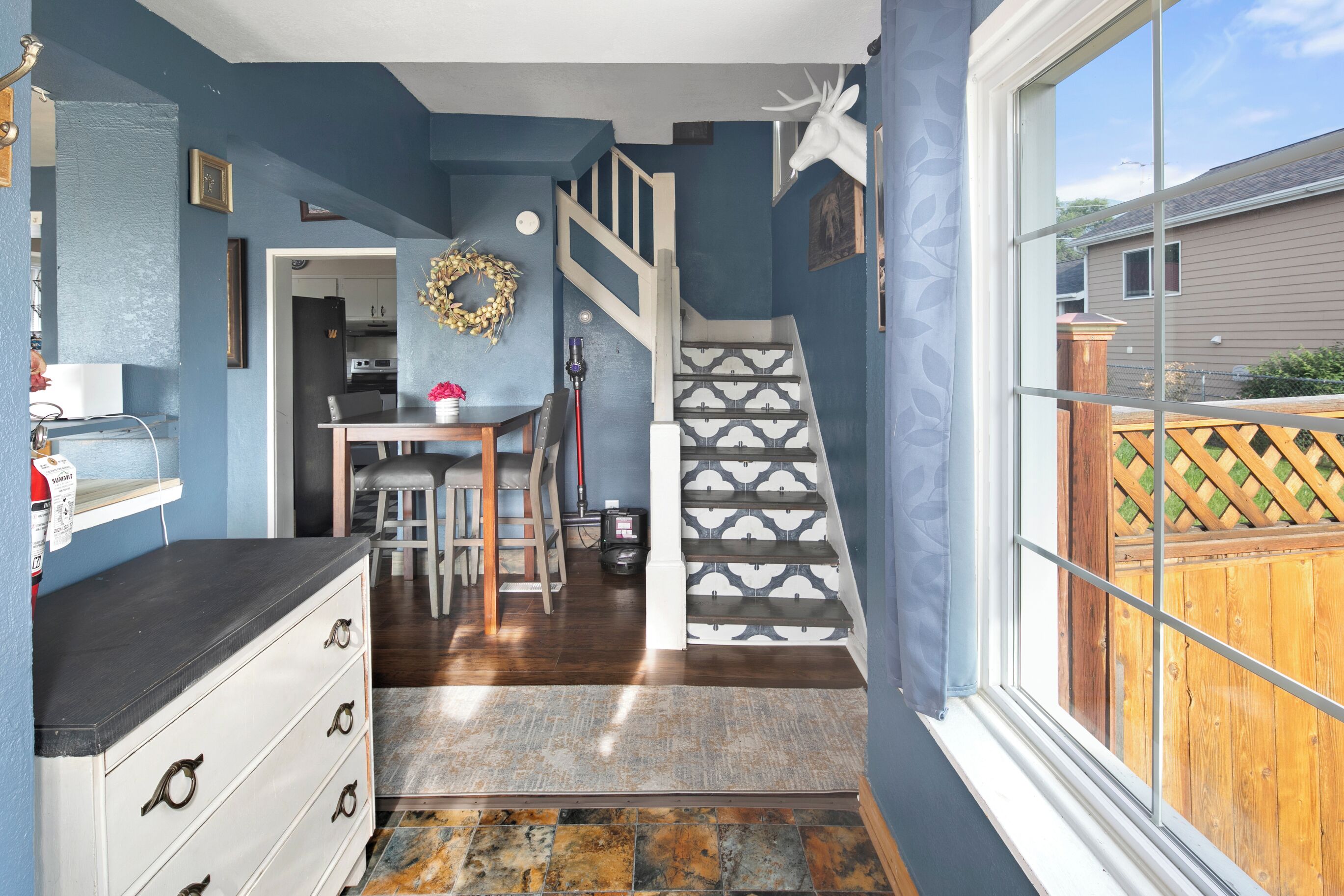 A room with a kitchen, dining area, and a staircase leading to another level.