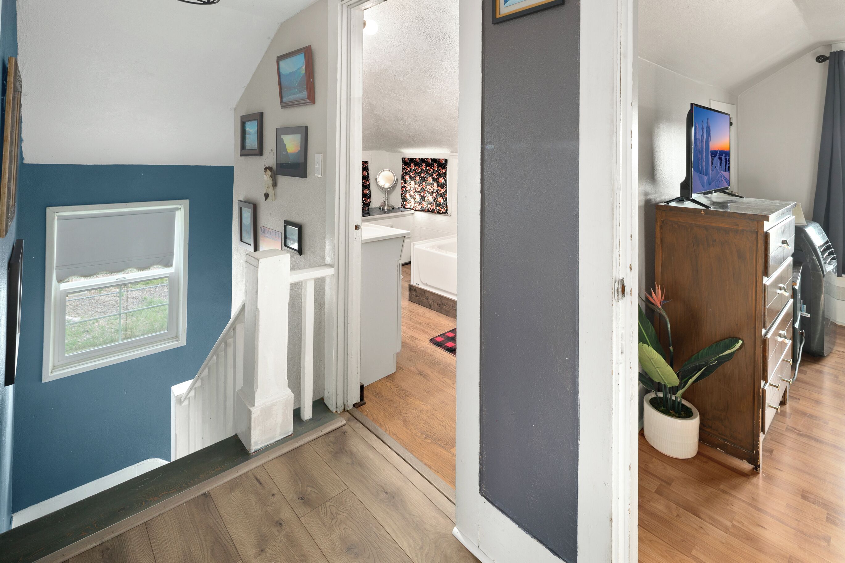 A hallway leading to a bathroom with a shower, a sink, and a mirror. There is a wooden cabinet with a television on top.