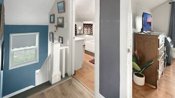 A hallway leading to a bathroom with a shower, a sink, and a mirror. There is a wooden cabinet with a television on top.