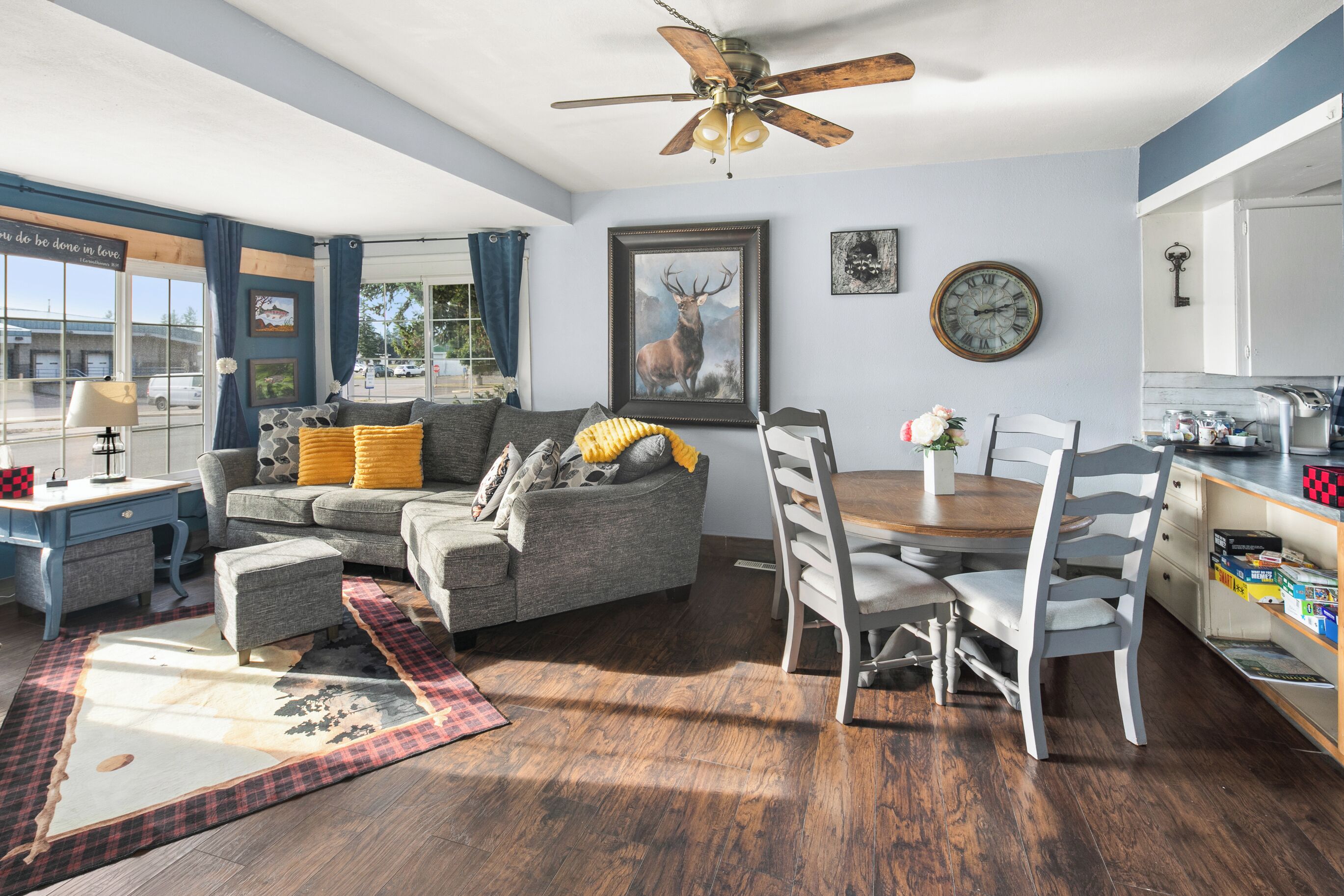 A modern living room with a grey sofa, a wooden dining table, and a ceiling fan.