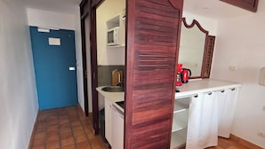 Una habitación con puerta azul, lavamanos blanco, cafetera roja y espejo sobre el mostrador.