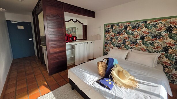 A hotel room with a bed, a desk with a red coffee maker, a mirror, and a wall with a tropical leaf pattern. - CLEMARA EVASION - Suite Azur  (La Trinité)