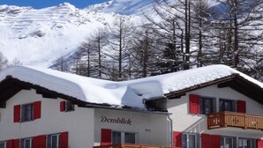A multi-story building with red shutters, a sign reading 'Domblick,' and a snowy mountain backdrop. - Domblick Appartement/Fewo 4-Bettwohnung Nr. 2 by Interhome (Saas-Fee)