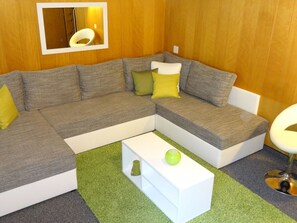 Un salon moderne avec un canapé d’angle, une table basse blanche et un tapis vert.
