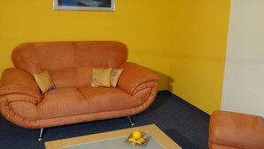 A room with a single orange sofa, a small table with a yellow ornament, and a framed picture on the wall. - Domblick Appartement/Fewo 4-Bettwohnung Nr. 2 by Interhome (Saas-Fee)