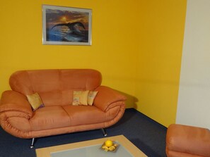 A room with a single orange sofa, a small table with a yellow ornament, and a framed picture on the wall. - Domblick Appartement/Fewo 4-Bettwohnung Nr. 2 by Interhome (Saas-Fee)