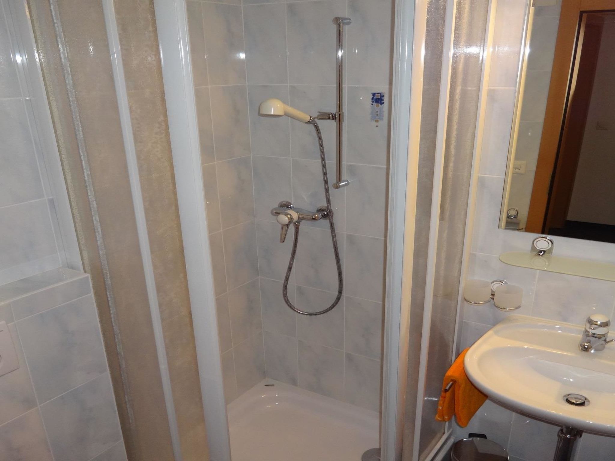 Ein Badezimmer mit einer Duschkabine, einem Waschbecken mit Spiegel und einem Handtuchhalter.