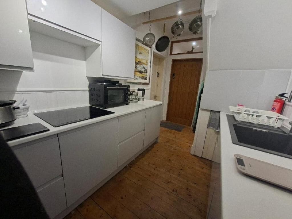 Una cocina con armarios blancos, microondas, estufa y piso de madera.
