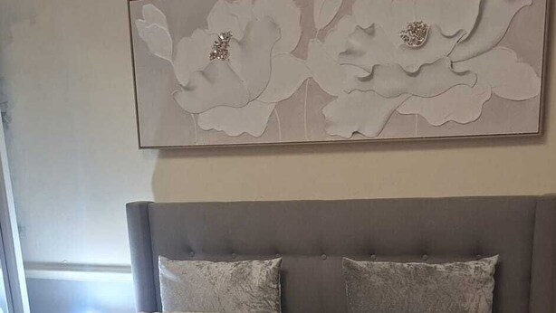 Un dormitorio con una cama grande, un cabecero con un panel decorativo y una ventana con cortinas.