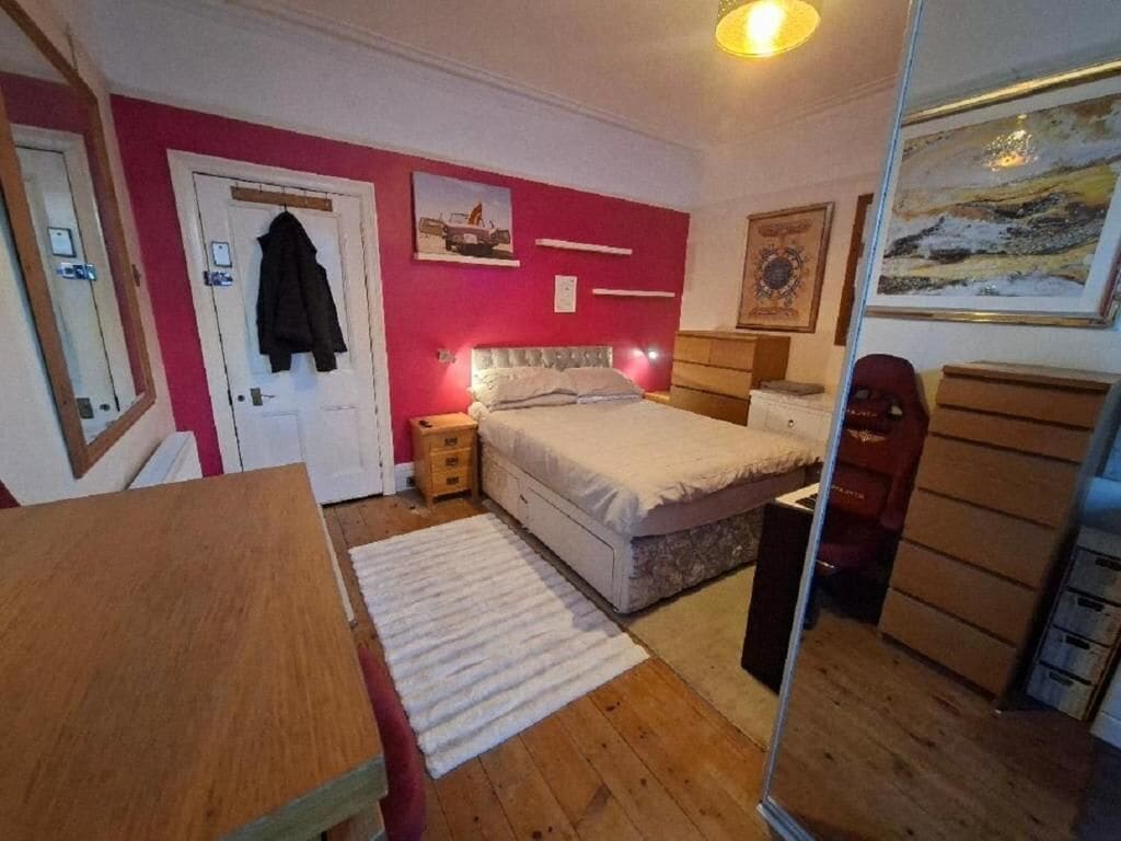 Een slaapkamer met een bed, een dressoir, een spiegel en een deur.