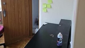 Una habitación con una puerta de madera, una mesa negra con una lata de bebida y notas adhesivas en la pared.