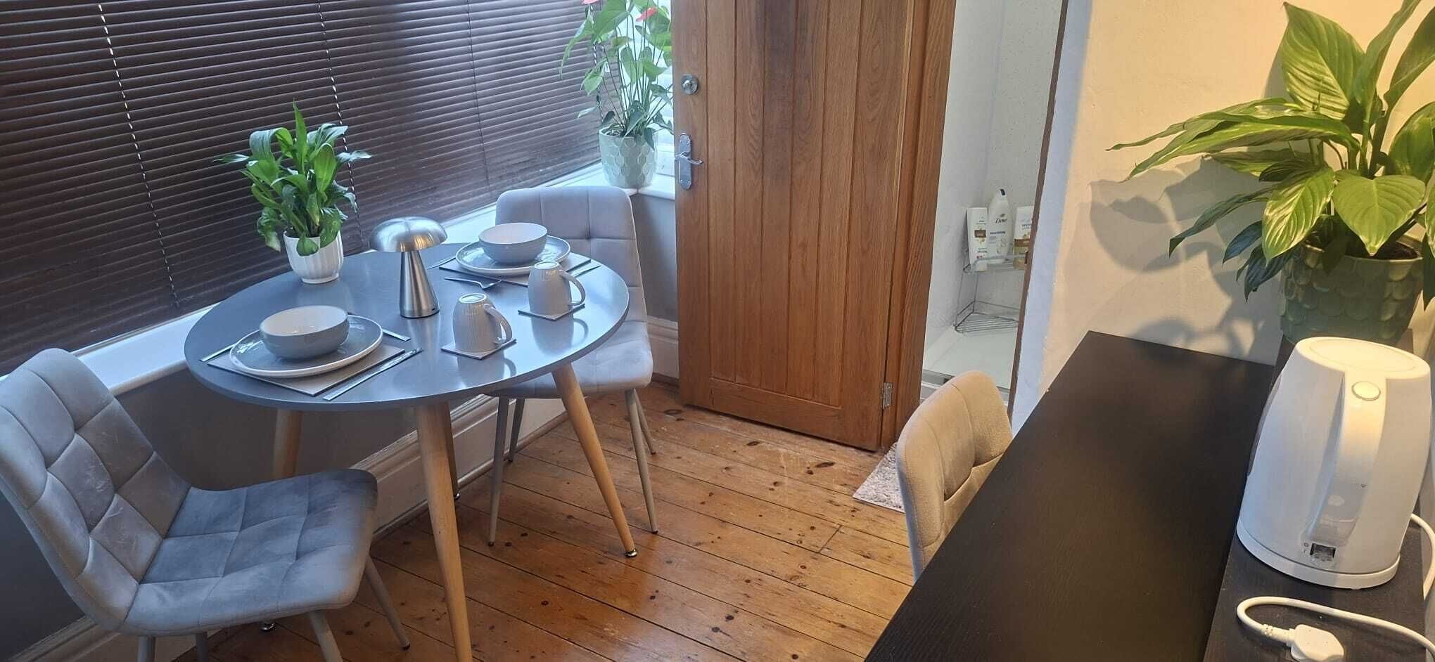 Un comedor pequeño con una mesa redonda, dos sillas, una cafetera y plantas en macetas.