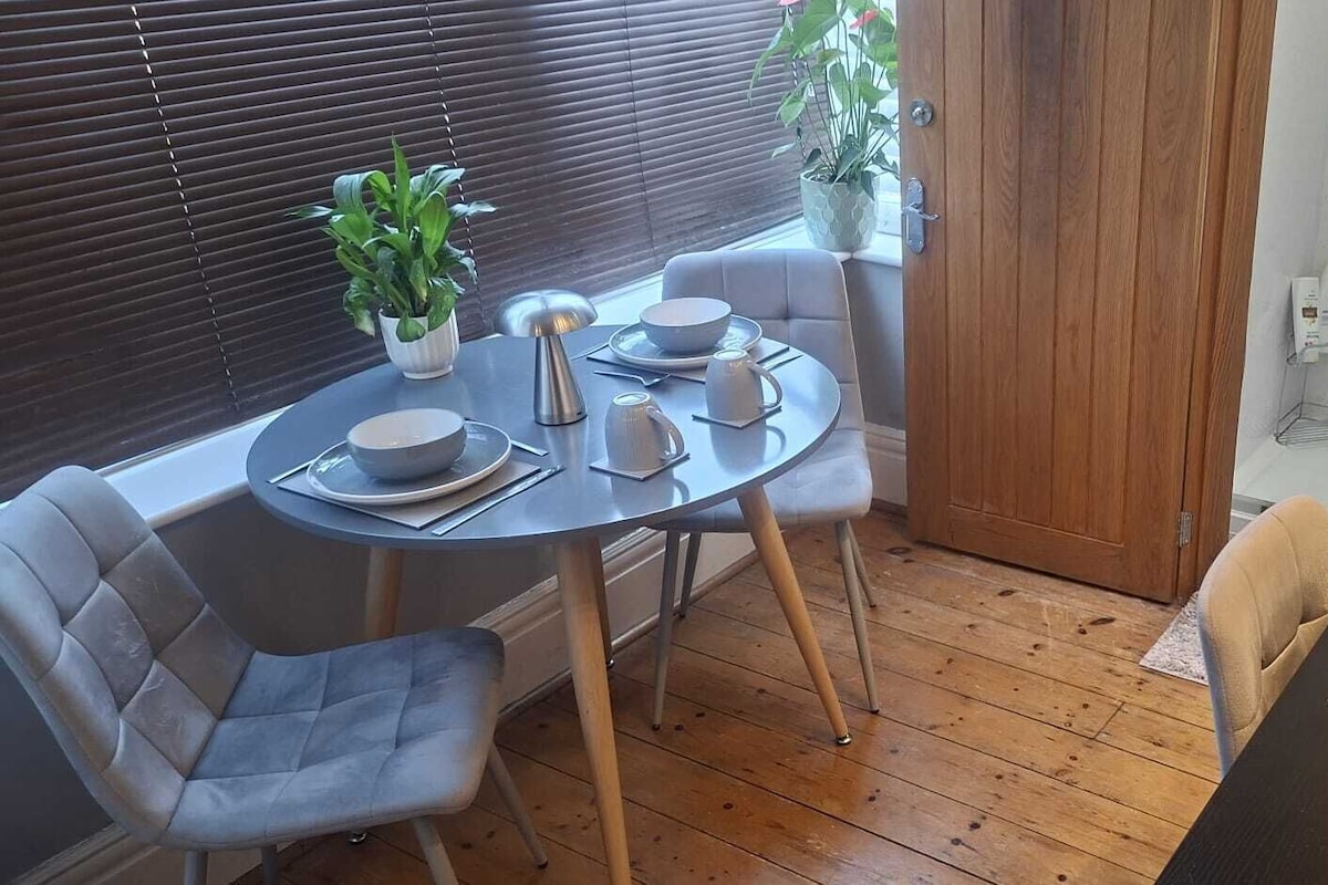 Ett litet, avskilt matområde med ett runt bord, två stolar, en kaffebryggare och krukväxter.