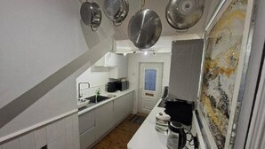 Cocina pequeña con gabinetes blancos, un lavamanos, una estufa y ollas colgantes.