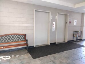 A hallway with a bench, two doors, a fire alarm panel, and a small bookshelf. - 2-bedroom condo Myrtle Beach with Waterway Views (Myrtle Beach)