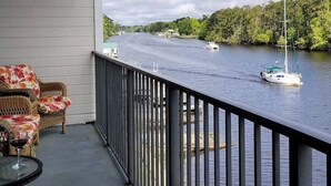 A balcony with wicker furniture and a glass table, overlooking a river with boats and greenery. - 2-bedroom condo Myrtle Beach with Waterway Views (Myrtle Beach)