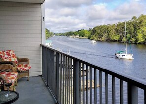 A balcony with wicker furniture and a glass table, overlooking a river with boats and greenery. - 2-bedroom condo Myrtle Beach with Waterway Views (Myrtle Beach)