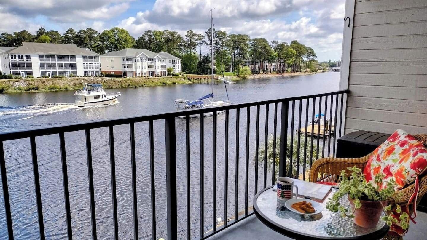 Un balcón con vista a un río, una embarcación y edificios al fondo.