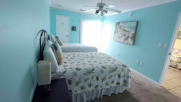 A bedroom with a bed, a ceiling fan, a door, and a painting on the wall. - 2-bedroom condo Myrtle Beach with Waterway Views (Myrtle Beach)