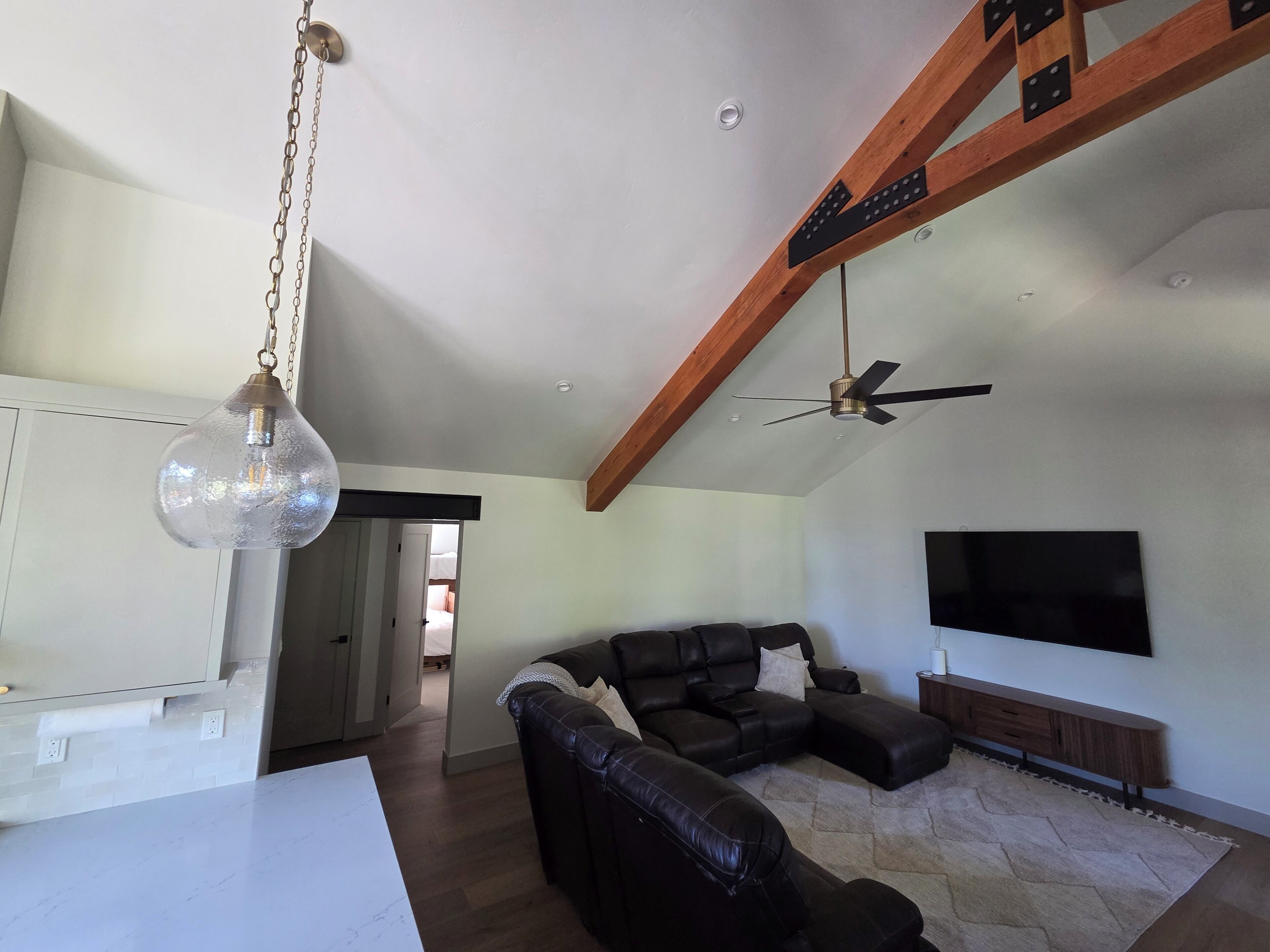 Una sala de estar con un sofá modular, un televisor montado en la pared, un ventilador de techo y una lámpara colgante.