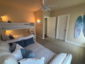 Ein Schlafzimmer mit Etagenbett, Deckenventilator, Surfbrett an der Wand und einer Tür zu einem weiteren Raum.