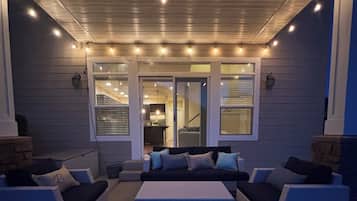 An outdoor seating area with two couches and a coffee table, under a covered patio with string lights.