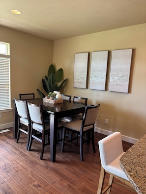Un coin repas avec une table en bois foncé entourée de chaises, une plante en pot et trois tableaux abstraits accrochés au mur.