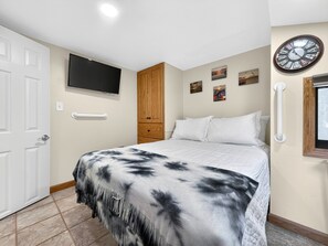 A bedroom with a bed, a TV, a clock, and artwork on the wall. - Key Largo Tiny House, Marina, Beach + Pool Access (Key Largo)