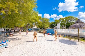 A beach volleyball court with players, a thatched-roof structure, and a fenced area with a white fence. - Key Largo Tiny House, Marina, Beach + Pool Access (Key Largo)